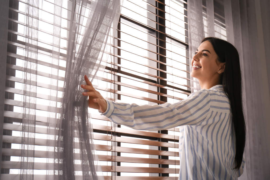 Woman opening window curtain at home in morning