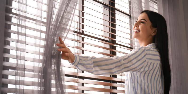Woman opening window curtain at home in morning